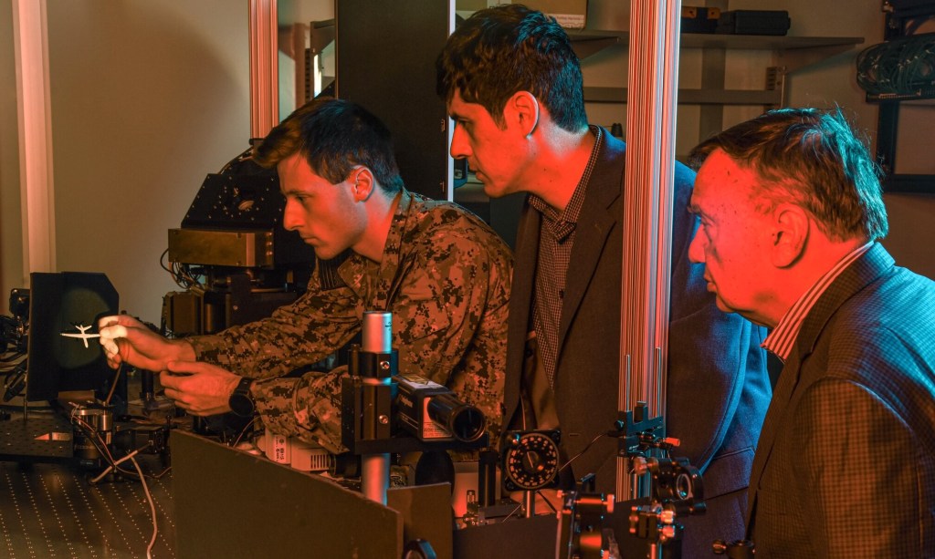 Naval Postgraduate School faculty researchers Brij Agrawal, right, and Leonardo Herrera, center, observe U.S. Navy Ensign Nicholas Messina as he positions a Reaper drone model in an optical beam path that simulates how a laser weapon system engages a distant flying drone. (Javier Chagoya)