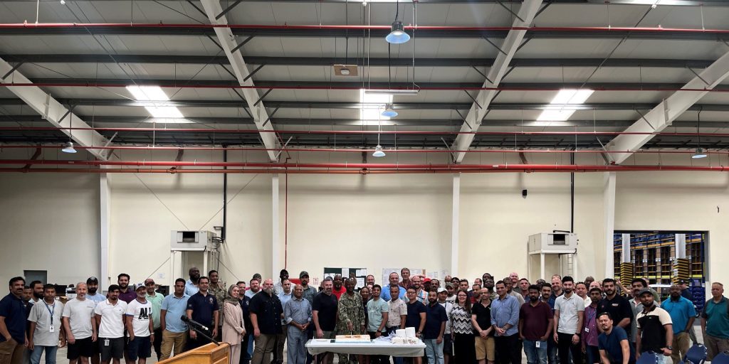 Navy Cmdr. John Olabode, Defense Logistics Agency Distribution Bahrain Commander, surrounded by his workforce and members of the DLA warehouse management system team, cuts a ceremonial cake to signal the new DLA WMS is live, Aug. 23, 2023.