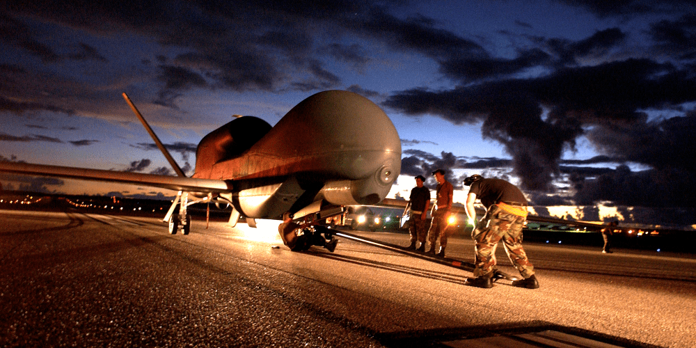Image of several Department of Defense personnel inspecting an unmanned aircraft on a runway.